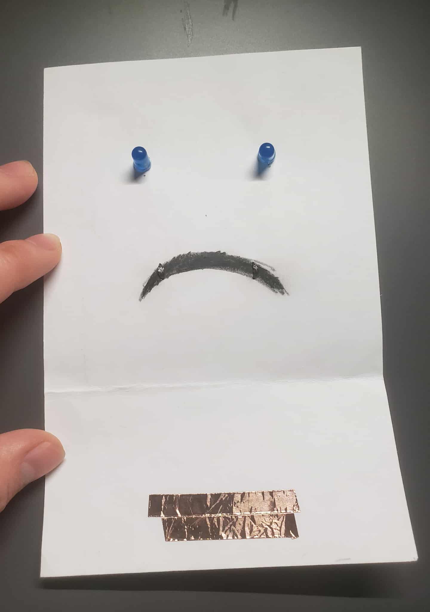 The front side of the smiley face circuit. The copper tape touches the conductive threats, closing the circuit 